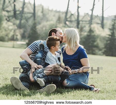 Stock Photograph - A family with young children playing in a park, with the mother and father kissing; Edmonton, Alberta, Canada. Fotosearch