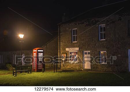 A lamp post illuminates a red telephone booth and bench outside a retail store; Bamburgh, Northumberland, England View Large Photo Image Picture - A lamp post illuminates a red telephone booth and bench outside a retail store; Bamburgh, Northumberland, England. Fotosearch