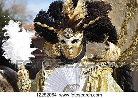 Picture - A person wearing an ornate gold and white costume with a fan and feather; Venice, Italy. Fotosearch