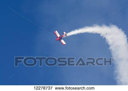 Stock Photo - A red and white aerobatic aircraft is pivoting and heading down smoke on; Rivadavia, Mendoza, Argentina. Fotosearch