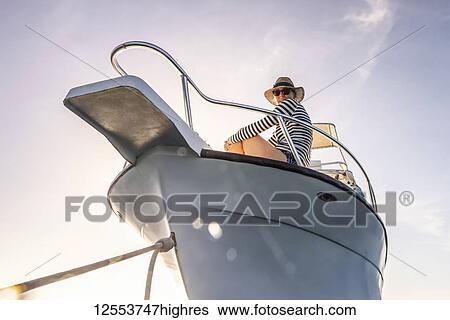 Stock Photograph - A woman wearing sunglasses and a sun hat looks down at the camera from the deck of a boat against a blue sky with sunlight; Bay Islands Department, Honduras. Fotosearch