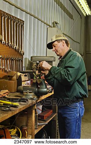 Stock Photo - Agriculture - A farmer works on machinery in his farm workshop / Iowa, USA.. Fotosearch