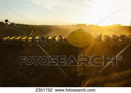 Stock Image - Agriculture - View from the rear window of a tractor cab of a John Deere 24-row planter planting corn in a conventionally tilled field at sunset / Minnesota, USA.. Fotosearch