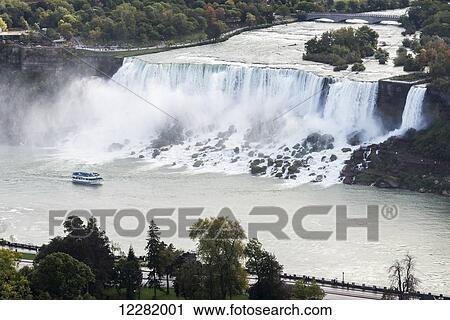 Stock Image - American Falls and a tour boat in Niagara River; Niagara Falls, New York, USA. Fotosearch