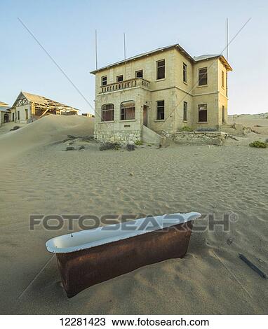 Stock Image - An old bathtub lying in the sand outside abandoned houses; Kolmanskop, Namibia. Fotosearch