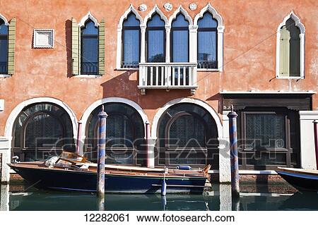 Stock Image - Boat moored along a building with arched windows; Venice, Italy. Fotosearch