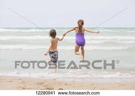 Stock Image - Boy and girl running on beach; Grand Bend, Ontario, Canada. Fotosearch