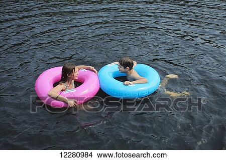 Boy and girl swimming with inflatable rings on Crystal Lake; Ontario, Canada View Large Photo Image Picture - Boy and girl swimming with inflatable rings on Crystal Lake; Ontario, Canada. Fotosearch
