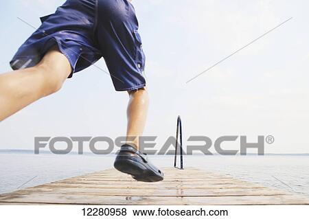Stock Photo - Boy running to jump off end of dock on Balsam Lake; Ontario, Canada. Fotosearch