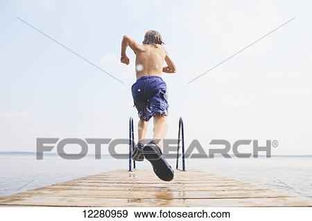 Stock Photo - Boy running to jump off end of dock on Balsam Lake; Ontario, Canada. Fotosearch