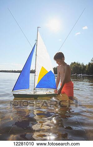Boy standing in lake playing with sailboat; Ontario, Canada View Large Photo Image Stock Image - Boy standing in lake playing with sailboat; Ontario, Canada. Fotosearch
