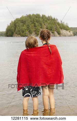 Stock Photography - Brother and sister wrapped in towel standing in Mara lake; Ontario, Canada. Fotosearch