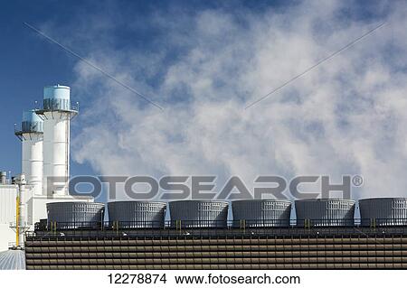 Close up of the steaming stacks of a cooling tower with stacks of an electrical power generation plant in background with blue sky; Alberta, Canada View Large Photo Image Picture - Close up of the steaming stacks of a cooling tower with stacks of an electrical power generation plant in background with blue sky; Alberta, Canada. Fotosearch