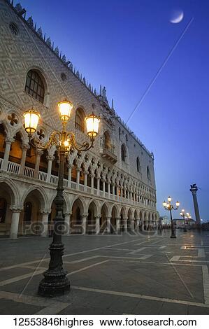 Stock Photograph - Doge's Palace at dusk with illuminated lamp posts and a moon in the blue sky; Venice, Italy. Fotosearch