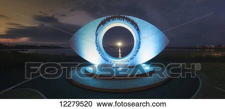 Stock Image - Eye sculpture illuminated with blue light at sunset; South Shields, Tyne and Wear, England. Fotosearch