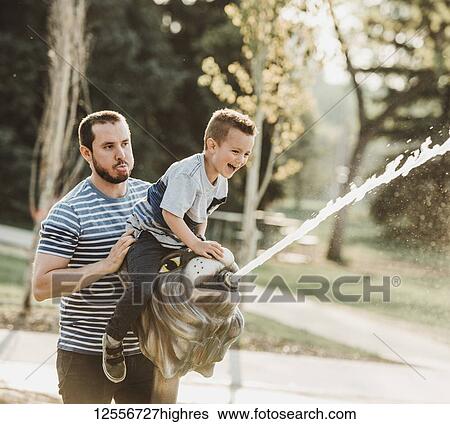 Stock Photograph - Father and young son at spray park; Edmonton, Alberta, Canada. Fotosearch
