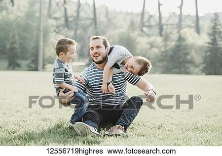 Stock Photograph - Father with young sons playing in a park; Edmonton, Alberta, Canada. Fotosearch