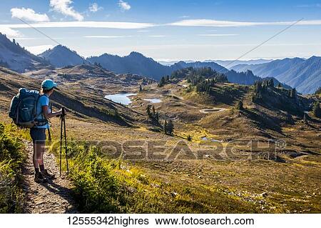 Stock Photograph - Female backpacker on High Divide Trail taking in the view of the Seven Lakes Basin in summertime, Olympic National Park, Olympic Mountains; Washington, United States of America. Fotosearch