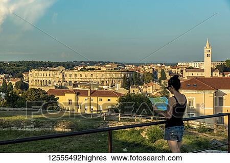 Stock Photograph - Female tourist with map at ancient Roman Amphitheatre known as Pula Arena; Pula, Istria, Croatia. Fotosearch