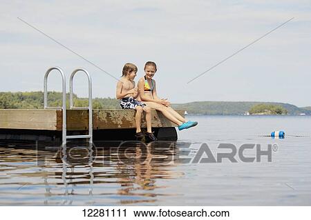 Girl and boy sitting at end of dock on Mara Lake; Ontario, Canada View Large Photo Image Stock Image - Girl and boy sitting at end of dock on Mara Lake; Ontario, Canada. Fotosearch