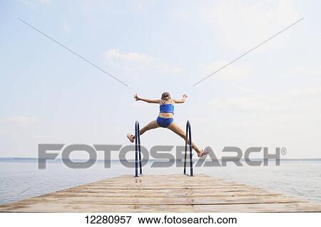 Stock Photo - Girl jumping off end of dock on Balsam Lake; Ontario, Canada. Fotosearch