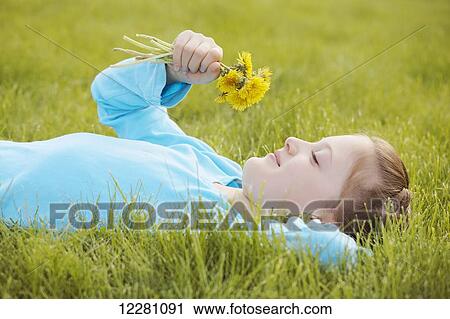 Stock Image - Girl laying down in grass holding bunch of dandelion flowers; Toronto, Ontario, Canada. Fotosearch