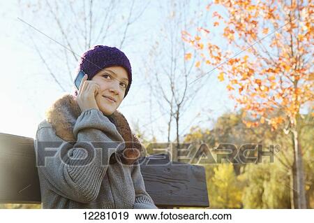 Girl sitting on park bench in autumn talking on smart phone; Toronto, Ontario, Canada View Large Photo Image Stock Photo - Girl sitting on park bench in autumn talking on smart phone; Toronto, Ontario, Canada. Fotosearch