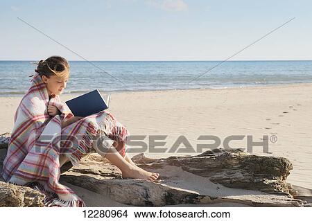 Girl wrapped in a blanket sitting on a log on beach reading a book; Toronto, Ontario, Canada View Large Photo Image Picture - Girl wrapped in a blanket sitting on a log on beach reading a book; Toronto, Ontario, Canada. Fotosearch