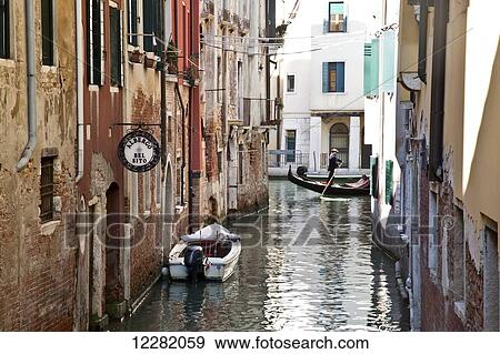Gondolier paddling on a canal between buildings; Venice, Italy View Large Photo Image Stock Photo - Gondolier paddling on a canal between buildings; Venice, Italy. Fotosearch