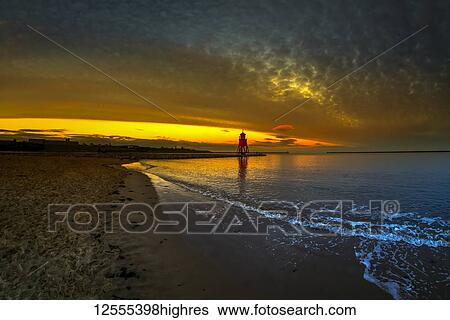 Stock Photograph - Herd Groyne Lighthouse backlit by a glowing, golden sunset; South Shields, Tyne and Wear, England. Fotosearch