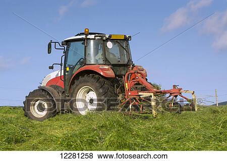 Stock Photo - Hill farmer spreading grass in hay meadow, with Steyr tractor, to dry out and make hay; Cumbria, England. Fotosearch