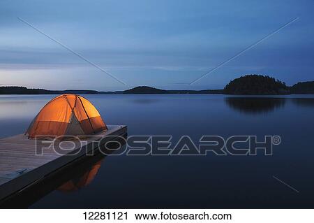 Stock Image - Illuminated tent on dock at sunset on Mara Lake; Ontario, Canada. Fotosearch