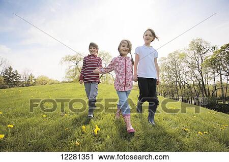 Stock Image - Kids holding hands walking through park; Toronto, Ontario, Canada. Fotosearch