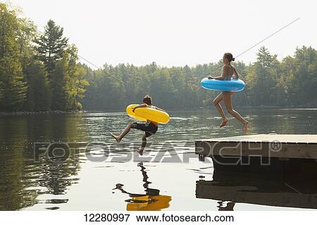 Kids jumping off end of dock holding inflatable rings on Crystal Lake; Ontario, Canada View Large Photo Image Stock Photo - Kids jumping off end of dock holding inflatable rings on Crystal Lake; Ontario, Canada. Fotosearch