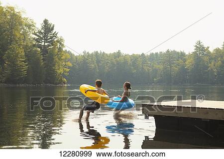 Kids jumping off end of dock holding inflatable rings on Crystal Lake; Ontario, Canada View Large Photo Image Stock Photo - Kids jumping off end of dock holding inflatable rings on Crystal Lake; Ontario, Canada. Fotosearch