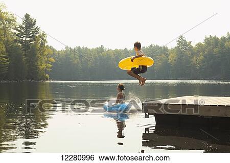 Kids jumping off end of dock holding inflatable rings on Crystal Lake; Ontario, Canada View Large Photo Image Stock Photograph - Kids jumping off end of dock holding inflatable rings on Crystal Lake; Ontario, Canada. Fotosearch