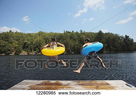 Kids jumping off end of dock holding inflatable rings on Crystal Lake; Ontario, Canada View Large Photo Image Stock Photography - Kids jumping off end of dock holding inflatable rings on Crystal Lake; Ontario, Canada. Fotosearch