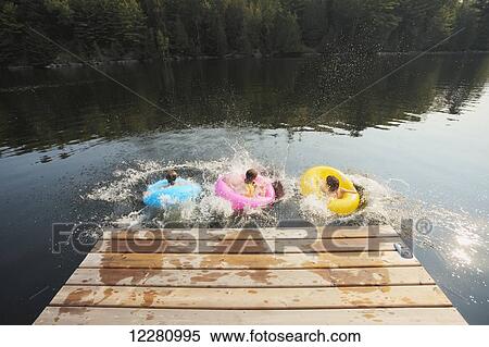 Kids jumping off end of dock holding inflatable rings on Crystal Lake; Ontario, Canada View Large Photo Image Stock Photography - Kids jumping off end of dock holding inflatable rings on Crystal Lake; Ontario, Canada. Fotosearch