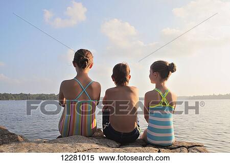 Stock Photography - Kids sitting on rock at edge of Crystal Lake; Ontario, Canada. Fotosearch