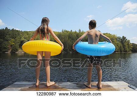 Stock Photo - Kids standing at end of dock holding inflatable rings on Crystal Lake; Ontario, Canada. Fotosearch