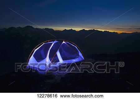 Stock Photograph - Light painting a backpacker tent high on mountaintop at sunset; Skagway, Alaska, United States of America. Fotosearch