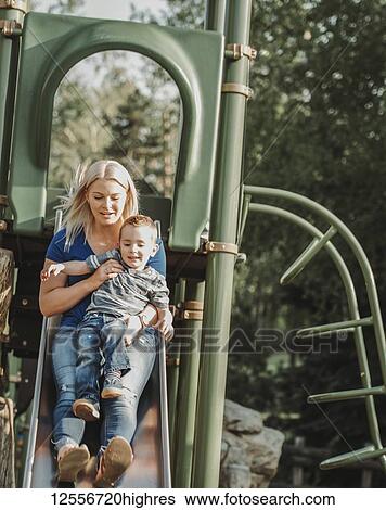 Stock Photograph - Mother on a slide with young son; Edmonton, Alberta, Canada. Fotosearch