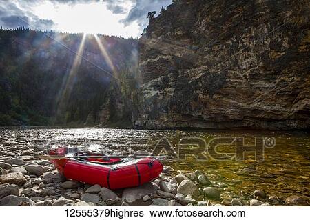 Stock Photograph - Packraft on the banks of the Charley River, sun going down behind ridge in background, Yukon-Charley Rivers National Preserve; Alaska, United States of America. Fotosearch