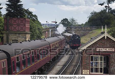 Stock Photo - Passenger trains traveling by Goathland station; Goathland, Yorkshire, England. Fotosearch