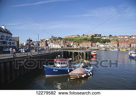 Pedestrians walk along a promenade and boats moored in the harbour; Whitby, North Yorkshire, England View Large Photo Image Stock Image - Pedestrians walk along a promenade and boats moored in the harbour; Whitby, North Yorkshire, England. Fotosearch