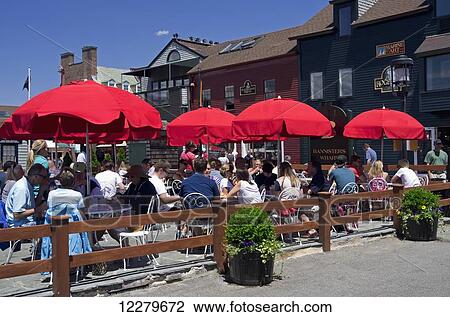 Stock Image - People at umbrella covered tables eating lunch at Black Pearl Restaurant, Bowen's Wharf; Newport, Rhode Island, United States of America. Fotosearch