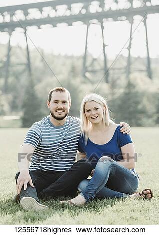 Portrait of couple in a park sitting on the grass with a bridge in the background; Edmonton, Alberta, Canada View Large Photo Image Stock Photograph - Portrait of couple in a park sitting on the grass with a bridge in the background; Edmonton, Alberta, Canada. Fotosearch