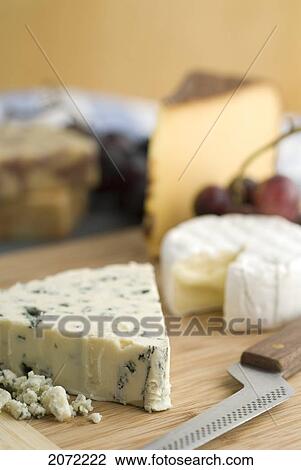 Stock Image - Selection Of Cheeses Including Blue Cheese, Brie And Gouda On Wood Board With Cheese Knife And Grapes. Fotosearch