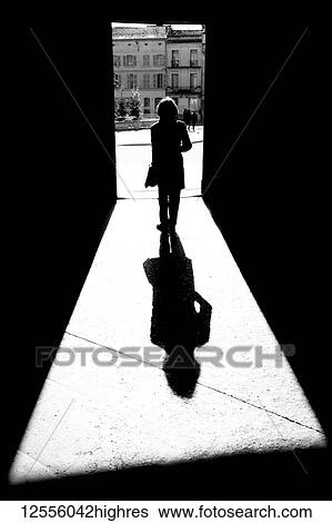 Stock Photograph - Silhouette and shadow of a woman going through a doorway to a town square towards City Hall; Arles, Provence Alpes Cote D'Azur, France. Fotosearch