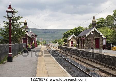 Stock Image - Small stone train station building with red lamp posts lining the train tracks; Garsdale, Yorkshire, England. Fotosearch